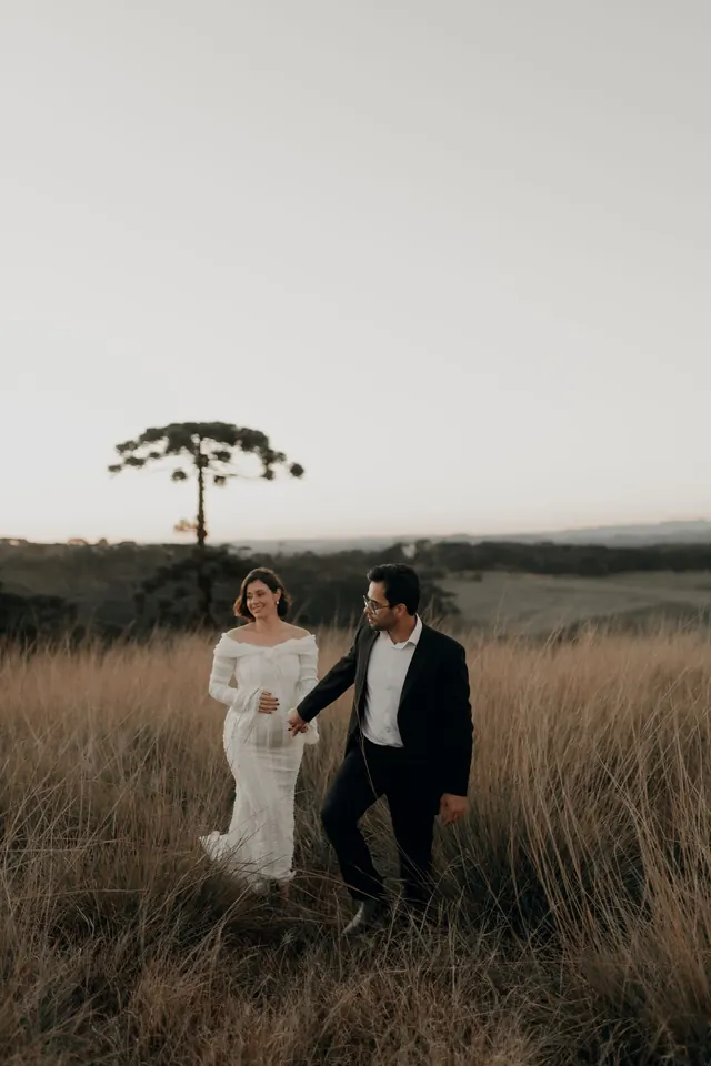 Casal caminhando no campo com uma araucária ao fundo