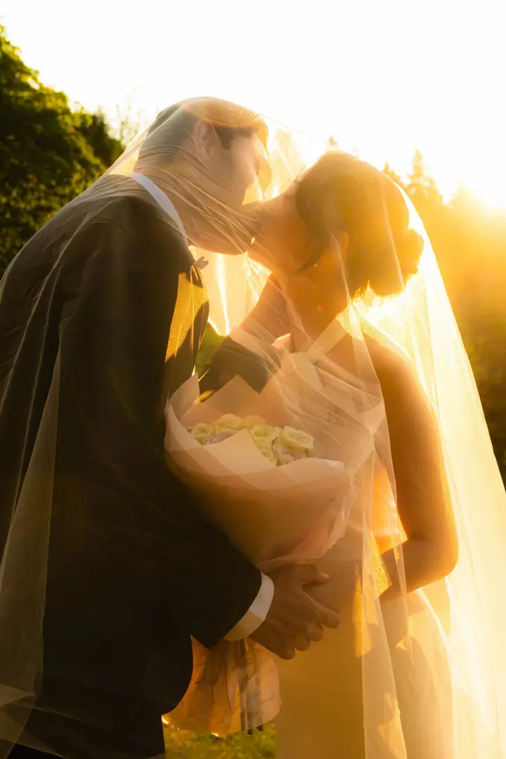 Casal se beijando sob o véu, contra a luz do fim de tarde